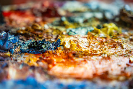 Close-up view of thick oil paint layers in blue, purple and orange tones on a messy palette. Captures abstract texture and creative energy of the painting process in a professional art studio..の写真素材