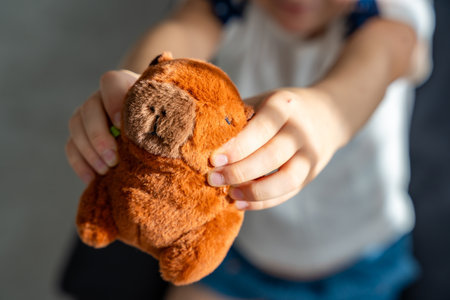 A plush capybara toy held in a child hands. The image reflects Gen Z love for internet-inspired mascots and the aesthetic comfort culture of soft toys. High quality photoの写真素材