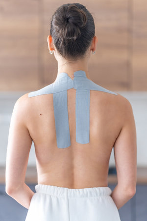 Kinesiology tape applied to the neck and shoulder area of a woman. Physical therapy and muscle...