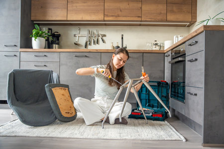 Young woman sitting on the floor assembling a chair with tools. Concept of female independence and do it yourself lifestyle. High quality photoの写真素材
