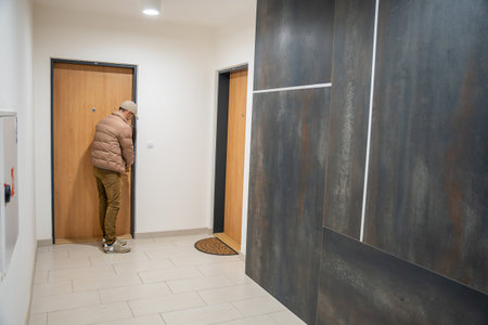Man bending down near the door inside a modern apartment hall. Waiting moment in residential corridor.の写真素材