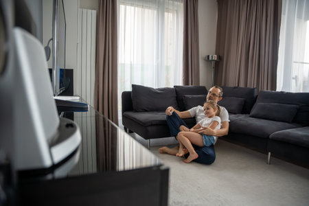 Father and daughter watching TV in the living room. Meaningful family leisure time at home.の写真素材