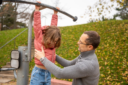 Man supporting his young daughter while she hangs from a horizontal bar. Muscle activity and playful...