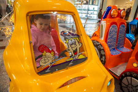 Little girl riding coin operated toy car attraction in shopping mall kids area. Childhood entertainment moment, family leisure activity and everyday fun experience in real life commercial environment.の写真素材