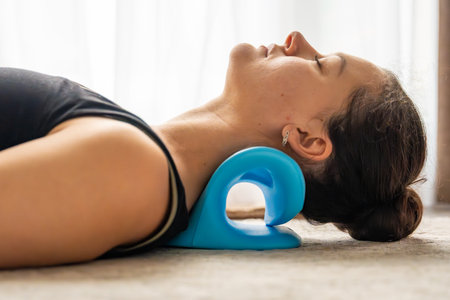 Young woman lies on the floor using a blue cervical traction device to stretch the neck. Home therapy for neck pain, muscle tension and spine decompressionの写真素材