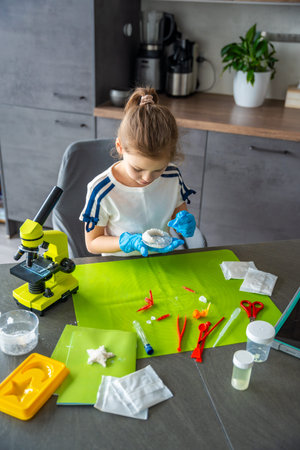 Young girl holding crescent shaped crystal grown at home and carefully examining its surface and...