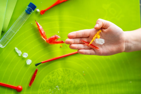 Close up of child hand holding colorful crystals of different shapes at home science table. Crystal...