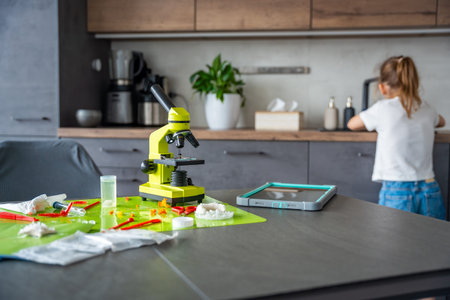 Home science experiment workspace with microscope and tools while child washing hands in background....