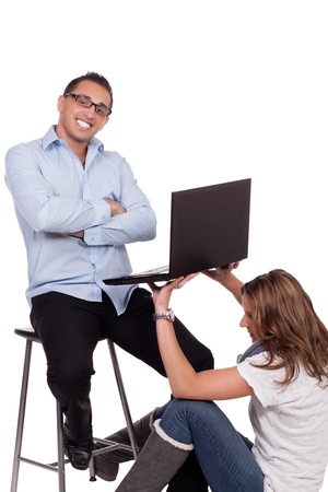 Humorous image of a business workstation with a businessman sitting with his arms folded and a broad grin as his assistant sits on the floor holding up his open laptop with her hands for him to workの写真素材