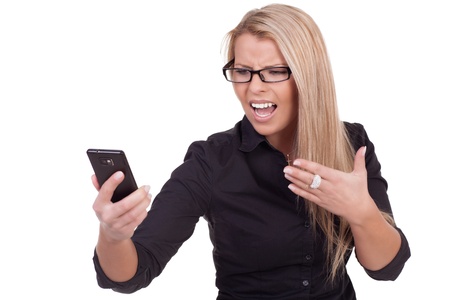 Frustrated woman wearing glasses looking at her mobile phone with a frown of dissatisfaction and disgust as she reads a message on the screen, half body portrait isolated on whiteの写真素材