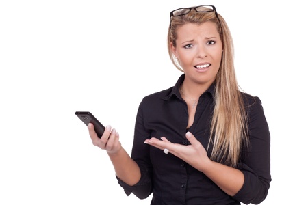 Upset woman with a confused expression frowning and pointing at her mobile or smartphone which she is holding in the other hand upper body studio portrait isolated on whiteの写真素材