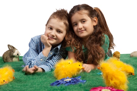Two happy young children lying on green grass surrounded by colourful yellow Easter chicks and an Easter bunnyの写真素材