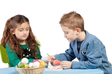 Attractive young brother and sister decorating Easter eggs sit at a table together working on a designの写真素材
