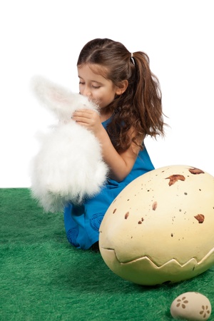 Easter theme with young girl sitting on the floor kissing her toy bunny with a huge egg beside her の写真素材