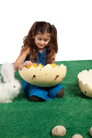Easter theme with young girl looking into egg shape with chicks inside and toy bunnies beside her の写真素材