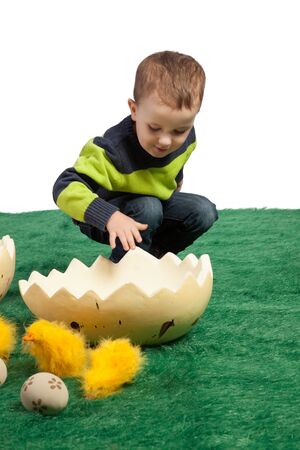Easter theme with small boy looking into the huge egg shape and toy chicks in foreground の写真素材