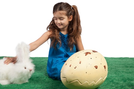 Easter theme with young girl sitting on the floor in a blue dress with a toy rabbit and a huge egg shapeの写真素材
