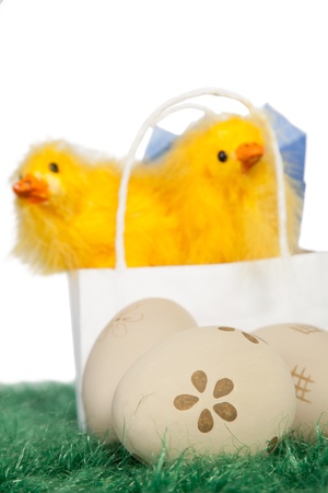 Paper bag with two yellow baby chicks and decorated Easter eggs on green grassの写真素材