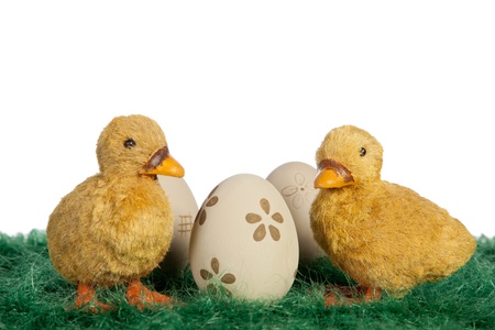 Two cute fluffy toy Easter ducklings standing on green grass on either side of a hand decorated Easter egg with a flower pattern against a white background with copyspaceの写真素材