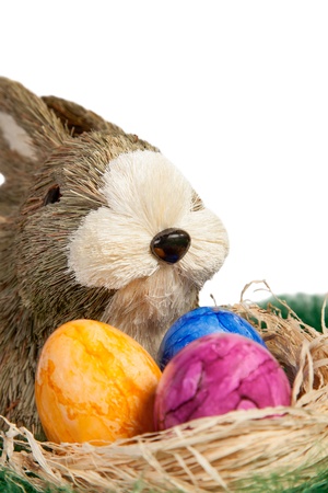 Face of a cute brown and white toy Easter Rabbit with a straw nest filled with handpainted colourful Easter Eggs with a marbled pattern over a white background for your seasonal greetingの写真素材