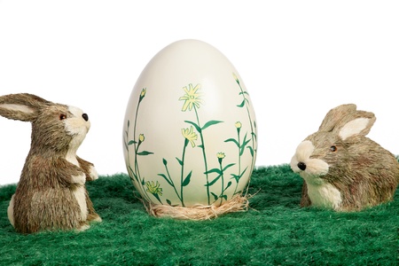 Two cute little furry brown toy Easter bunnies on green grass with a handpainted egg deorated with flowersの写真素材