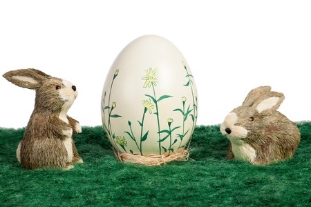 A single large handpainted Easter Egg with flowers flanked by two cute brown and white Easter bunnies on green grass with a white background and copyspaceの写真素材