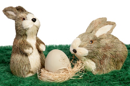 Pair of cute brown and white furry toy Easter bunnies watching over a single hand decorated Easter egg with a floral pattern on the traditional Easter Egg Huntの写真素材