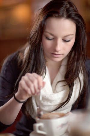 Beautiful young woman having a delicious after dinner cup of frothy cappuccino coffee in a restaurantの写真素材