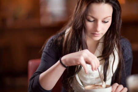 Beautiful stylish woman stirring a cup of fresh frothy cappuccino with copyspaceの写真素材