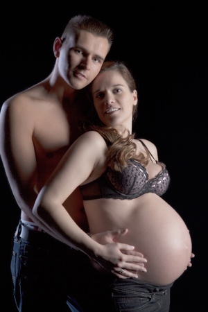 Young man holding tenderly from behind his beautiful pregnant wife, on black backgroundの写真素材