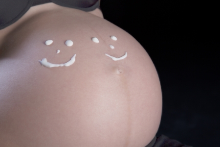 Pregnant woman with two smiley faces drawn on her very large belly signifying that she is expecting twins, cropped torso portraitの写真素材
