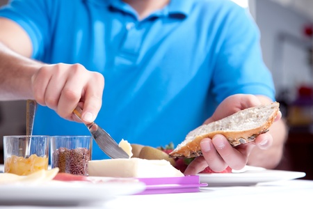 Low angle cropped view of the hands of a man buttering a slice of wholewheat bread at a breakfast table with pots of jam and marmalade alongsideの写真素材