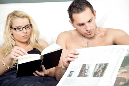 Attractive couple reading in bed together with the woman engrossed in her book while the man concentrates on his newspaperの写真素材