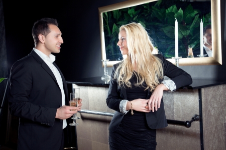 Romantic beautiful young couple in love staring into each others eyes as they stand in front of a fireplace with flutes of champagne on an elegant evening outの写真素材