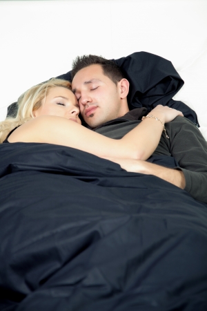 Loving young couple lying close together with their arms around each other enjoying a peaceful sleepの写真素材