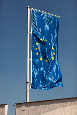 European union flag hoist on a metal flagpole against a blue skyの写真素材