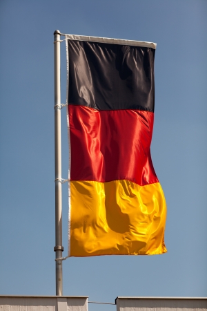 German national flag flying over a rooftop against a clear sunny blue skyの写真素材