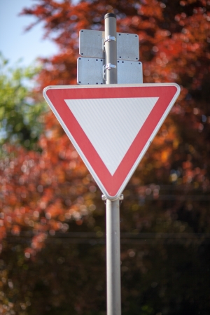 Triangular to yield to traffic on a metal pole against foliageの写真素材