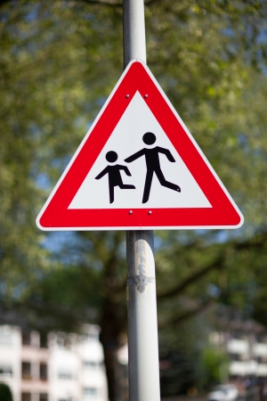 Traffic warning sign for children playing mounted on a pole in an urban environment against greenery telling motorists to slow down and be awareの写真素材