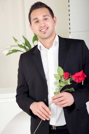 Smiling romantic young man about to propose to his girlfriend nervously holding a long stemmed red rose in his handsの写真素材