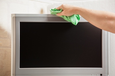 A housewife is cleaning the Television with a green duster.の写真素材