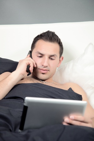 A Business Man is lying in a bed and watching to the Tablet PC during a phone call の写真素材