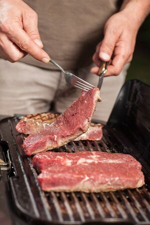 A man is turning a steak on a electric grill in his garden.の写真素材