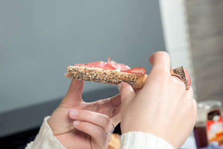 Closeup view of the hand of a young woman wearing a large ring eating a ham rollの写真素材