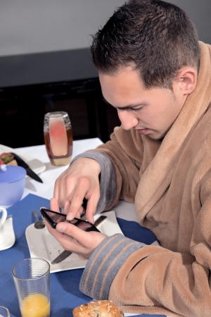 Closeup view of a man dressed in a dressing gown using his mobile at breakfast scrolling with his finger on the touchscreenの写真素材