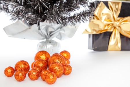 Some shiny christmas balls infront of a present and a X-Mas Tree on a white background の写真素材