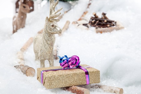 A golden reindeer is presenting a golden Christmas Gift in a snowy winter scene の写真素材