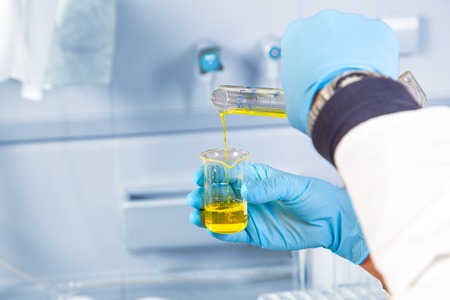 The analytical chemist is decanting a yellow dangerous liquid into an other test glass の写真素材