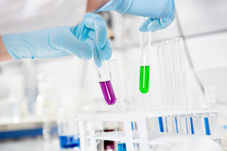 The Chemist takes up two test tubes with a  purple and green liquid の写真素材