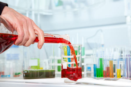 The Chemist Assistant is decanting a red liquid into a 200 milliliter beaker の写真素材